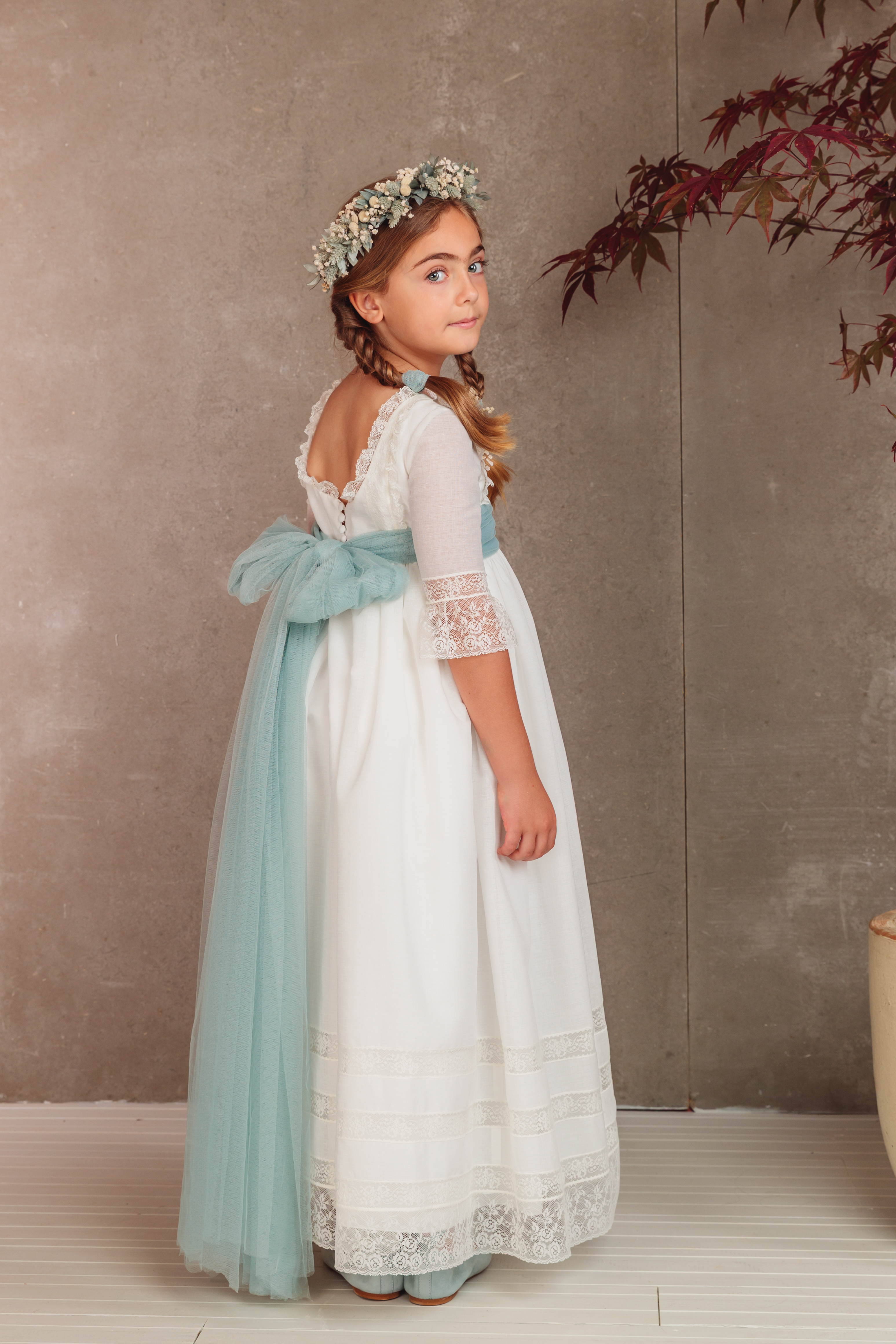 Vista trasera del vestido de comunión Covadonga con escote bailarina, lazada de tul verde agua y detalles de encaje. Colección 2026 Flor de C